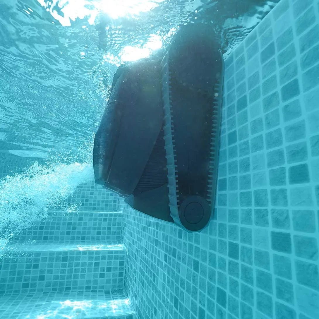Black robotic pool cleaner with a tracked design, gliding along the tiled wall underwater.