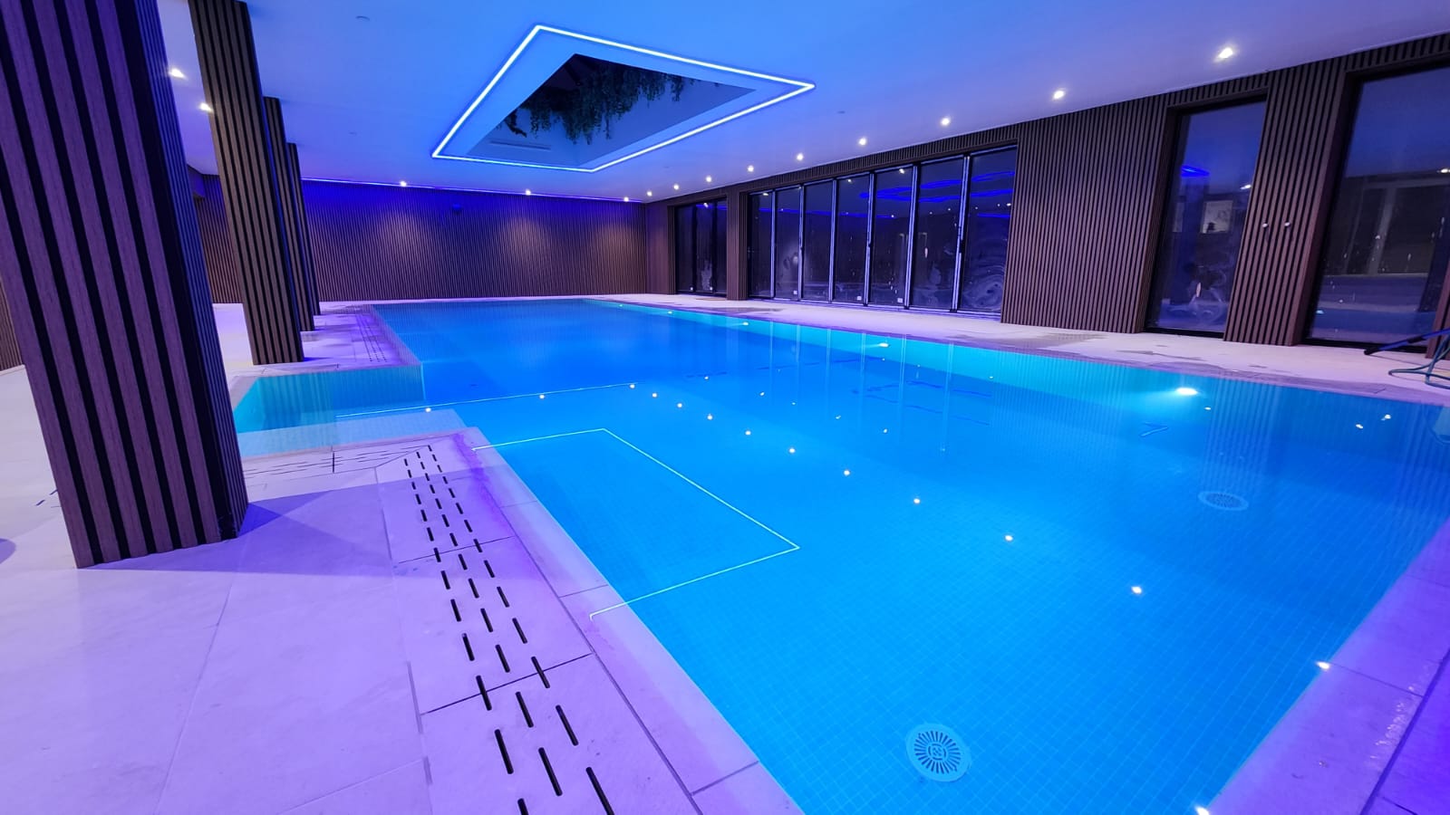 Blue illuminated indoor swimming pool with sleek modern design and dark wood paneling