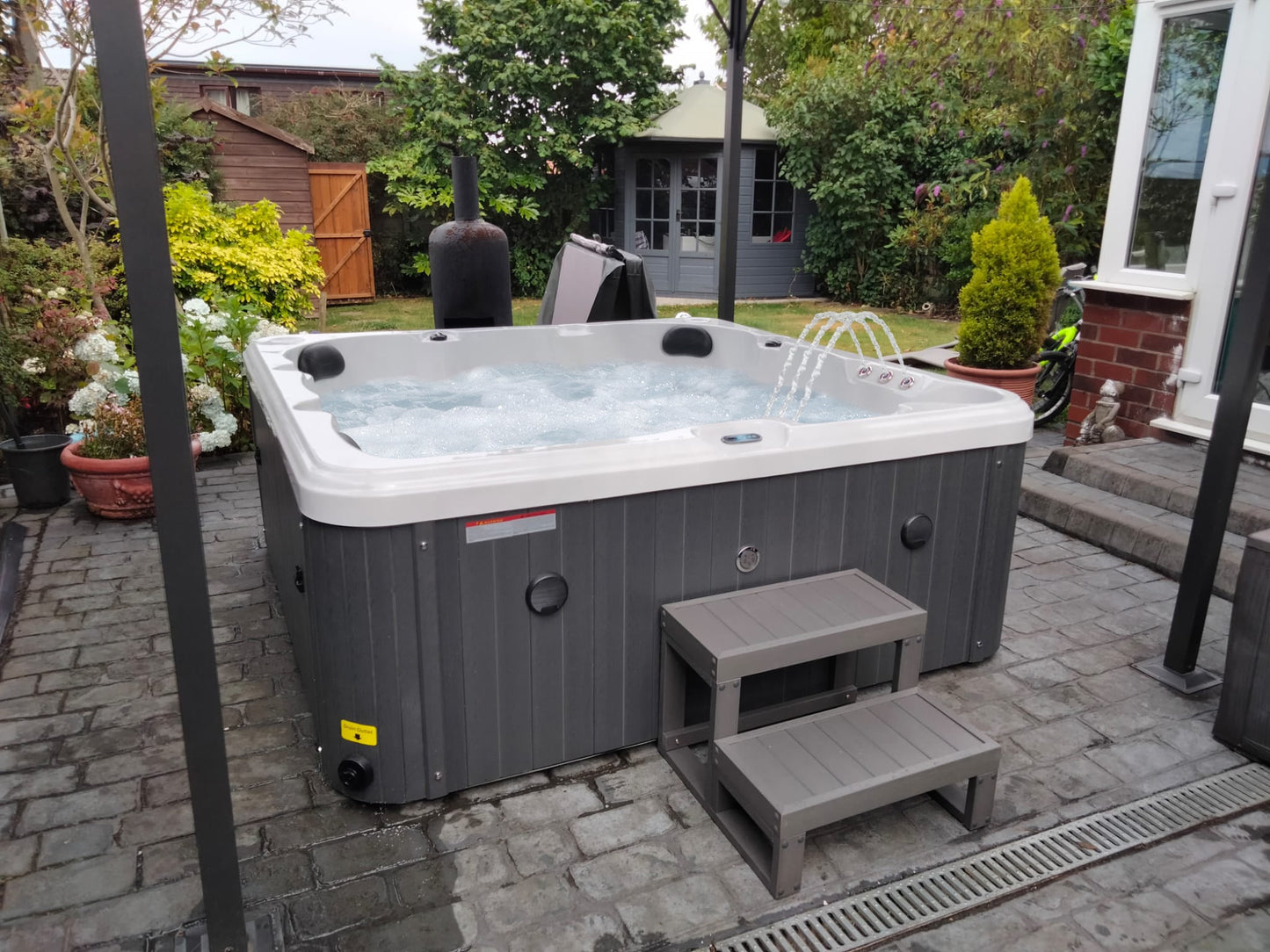 Gray and white hot tub with a built-in water feature spouting jets, featuring a modern design with vertical paneling on the exterior.