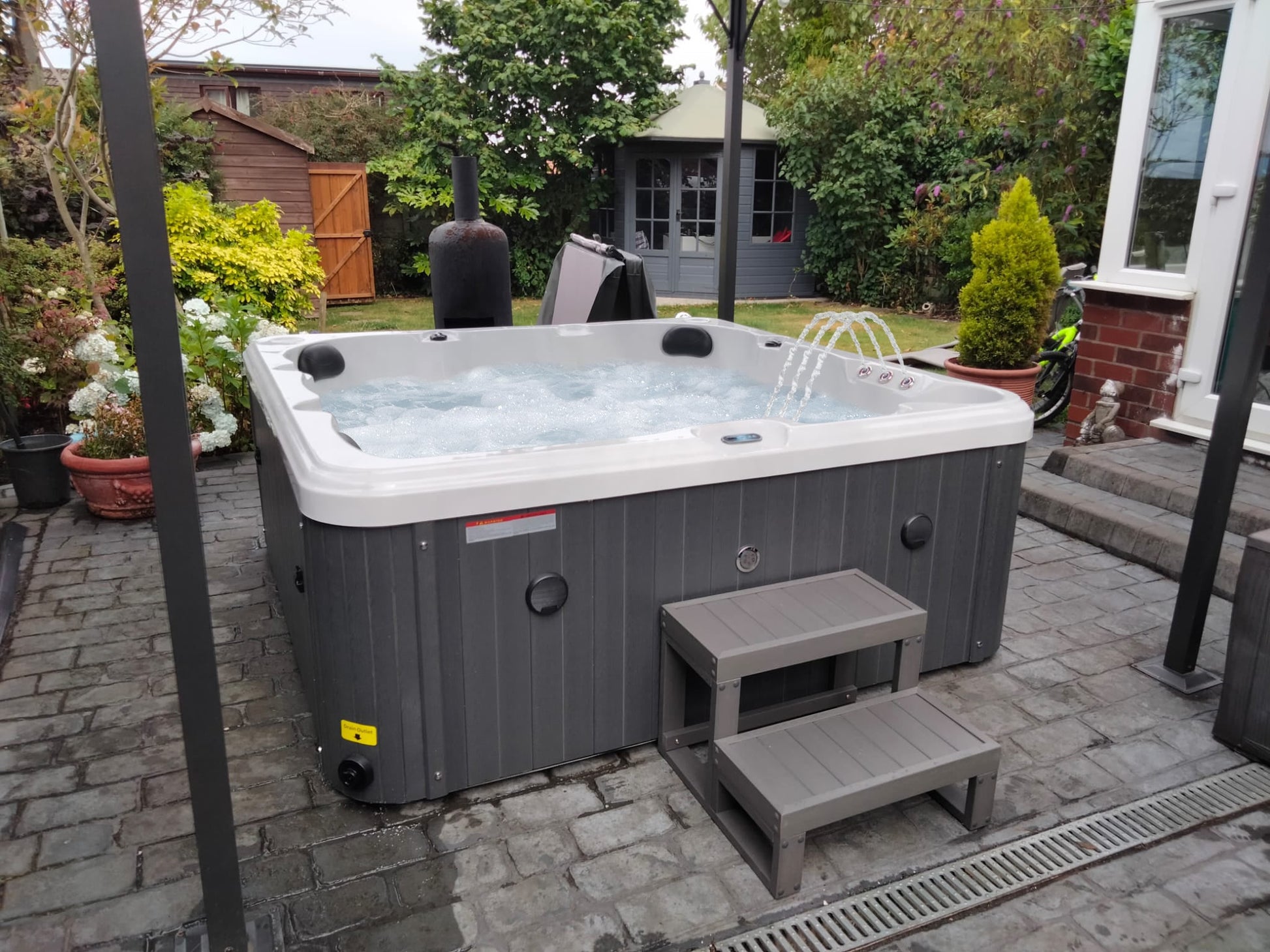 Gray and white hot tub with a built-in water feature spouting jets, featuring a modern design with vertical paneling on the exterior.