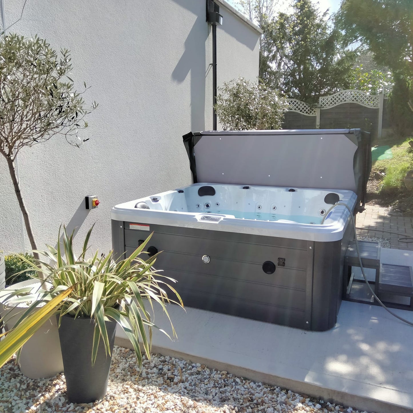 Gray and white hot tub with a hinged lid, featuring black circular jets along the interior edges.
