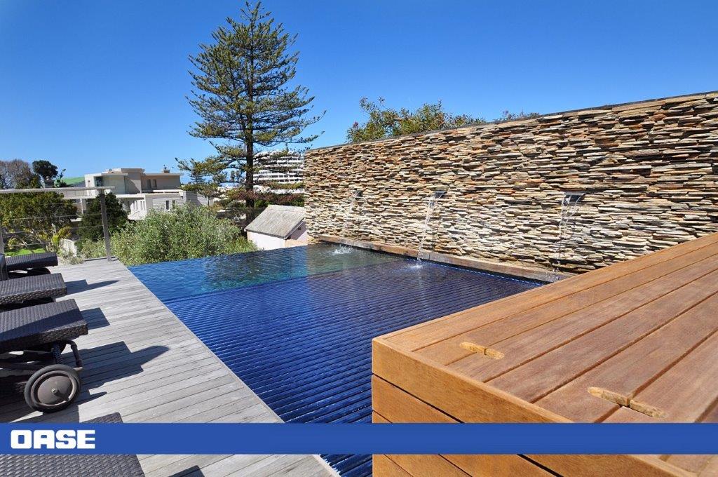 Infinite blue infinity pool with a stone waterfall feature and wooden deck.