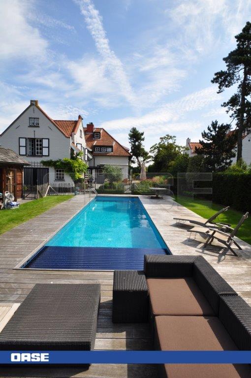 Rectangular in shape with clear blue water and a dark blue pool cover, surrounded by wooden decking and modern outdoor furniture.