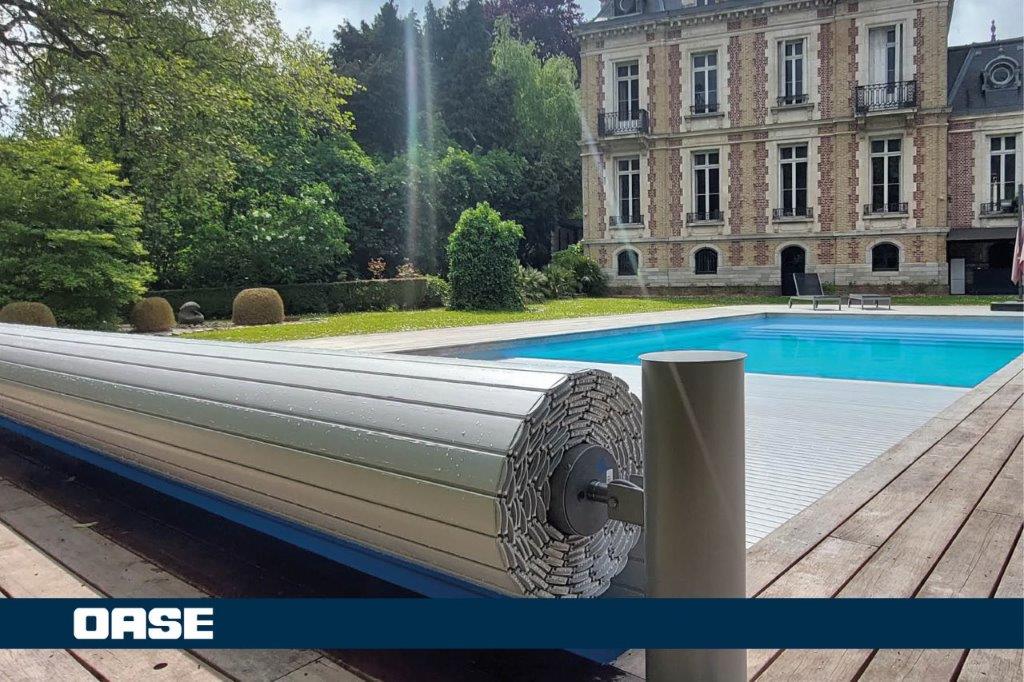 Silver metallic pool cover with a sleek, ribbed design and sturdy cylindrical roller mechanism.