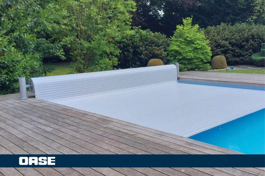 Silver oase pool cover with ribbed texture, partially rolled up over a blue swimming pool.