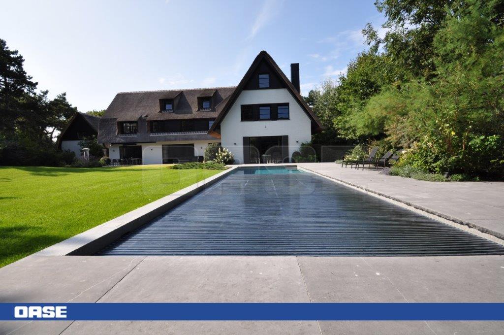 A long, rectangular in-ground swimming pool with dark blue water and a sleek black cover.