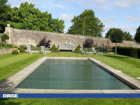 Rectangular in shape with clear green water, surrounded by neatly trimmed grass and stone walls.