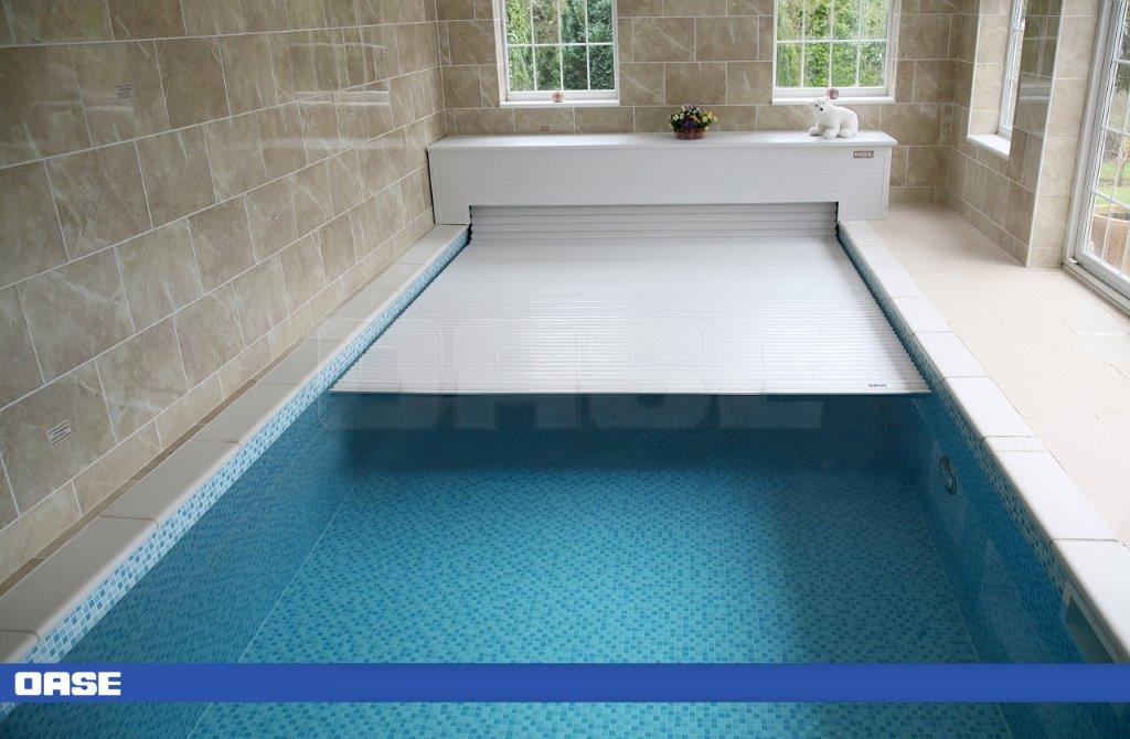 White retractable pool cover with a ribbed texture, installed over an indoor swimming pool.