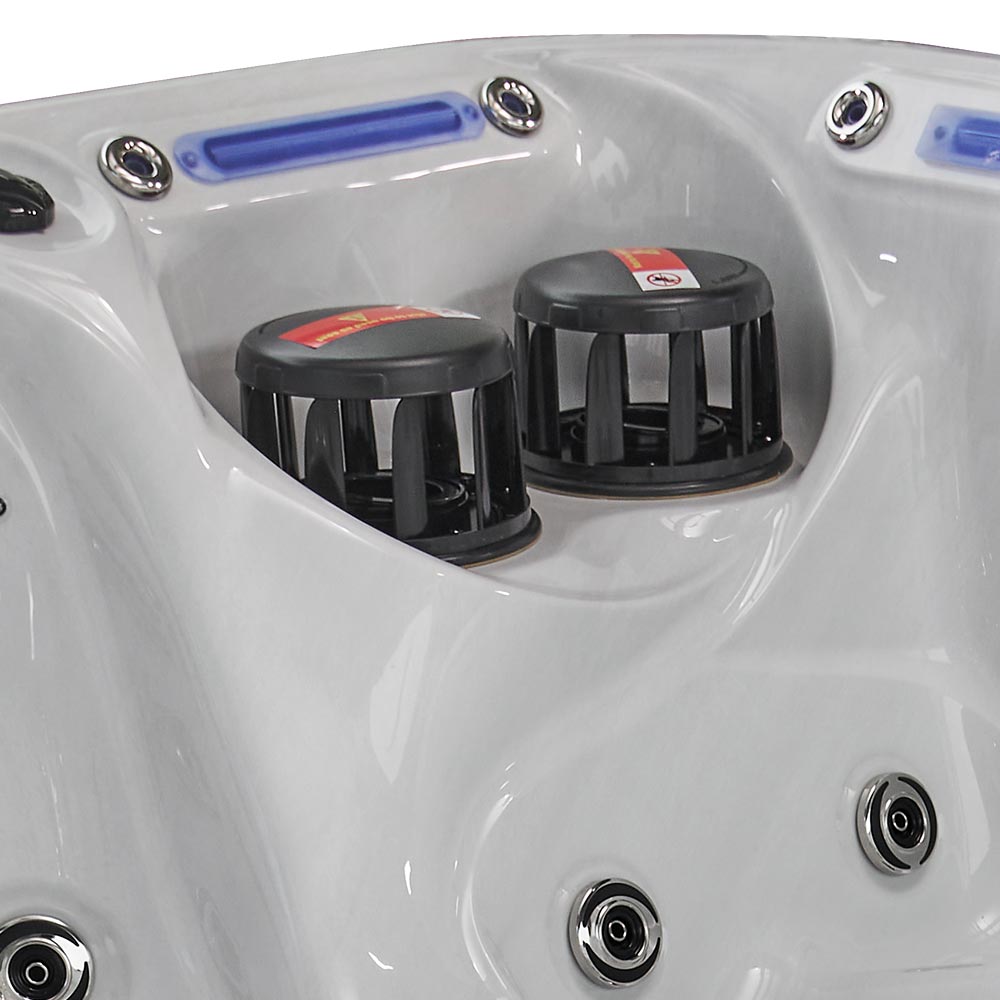 Black plastic jet nozzles with red warning labels sit inside the white molded surface of a hot tub.