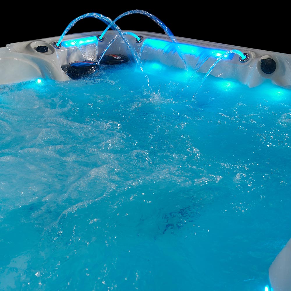 A white hot tub with blue led lighting and water jets spraying from the rim.