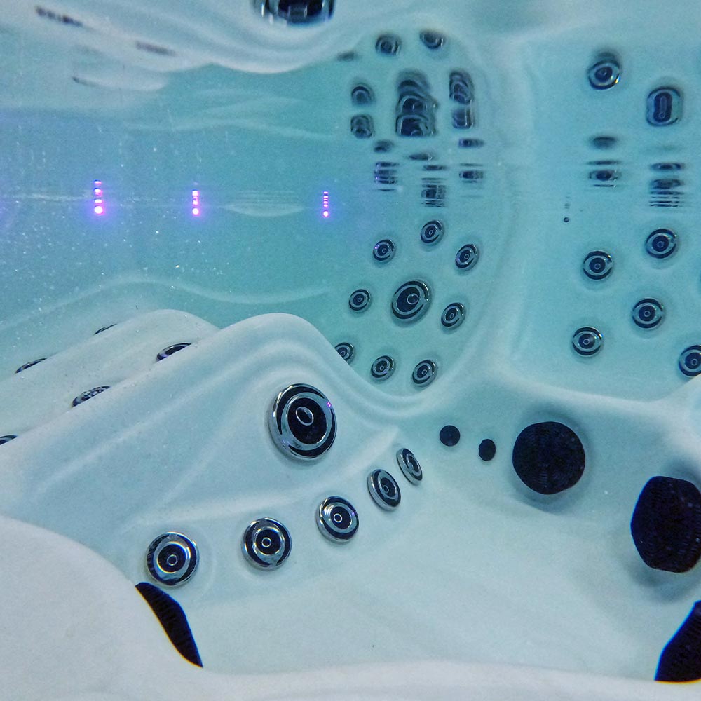 White hot tub with chrome jets and black accents, illuminated by purple led lights.