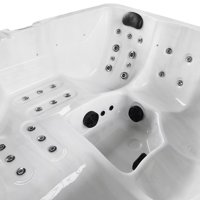 White hot tub with black jet nozzles and circular chrome fixtures.