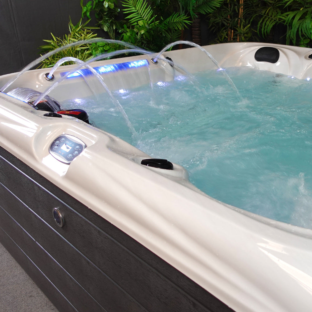 Cream-colored hot tub with black accents and blue led lighting, featuring curved water jets spraying into the clear turquoise water.