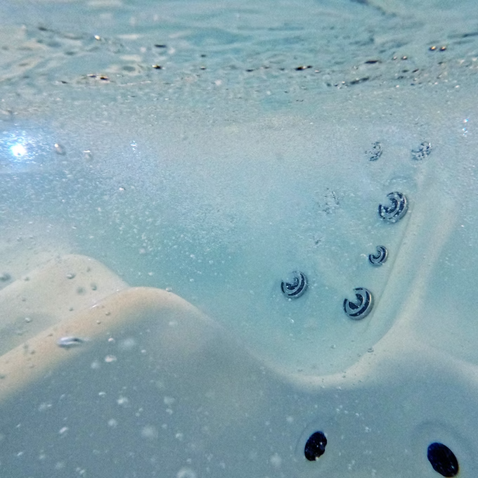 Blue-tinted water with silver circular jet nozzles and black drainage holes.
