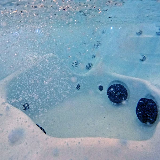 Blue water with bubbles and dark circular jets in a hot tub.