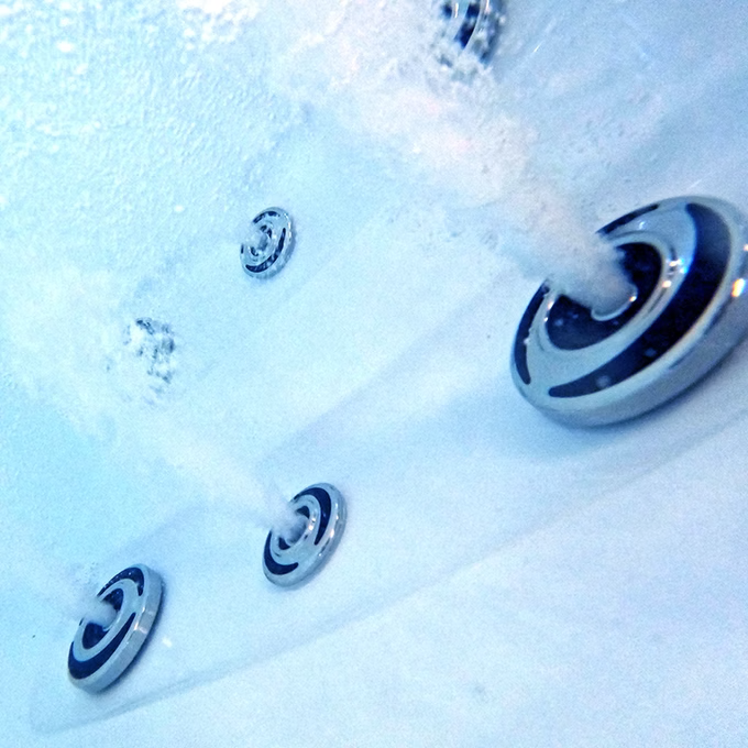 Chrome-finished whirlpool jet with black accent rings, embedded in a white spa surface.