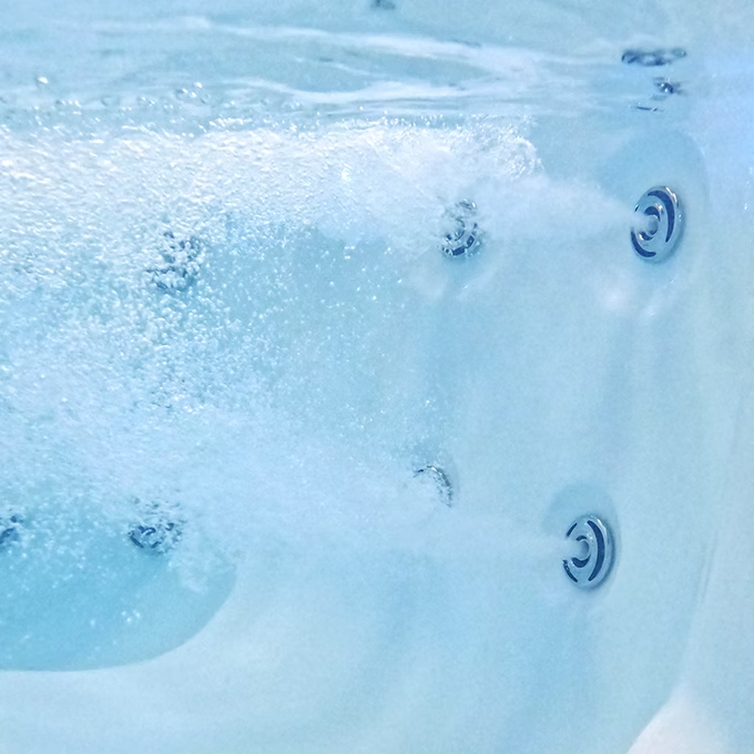 Light blue acrylic hot tub with silver jet nozzles bubbling water.